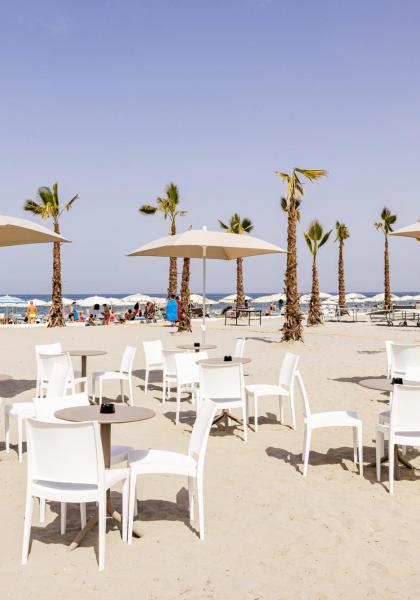 Spiaggia con palme, sedie bianche e ombrelloni.