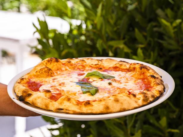 Pizza Margherita con basilico fresco su piatto bianco.