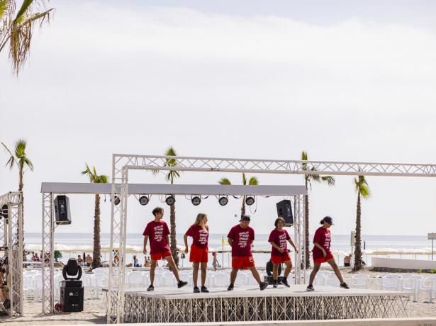 Danseurs sur scène de plage avec des t-shirts rouges.