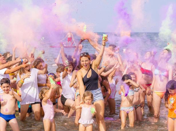 Persone festeggiano in spiaggia con polveri colorate.