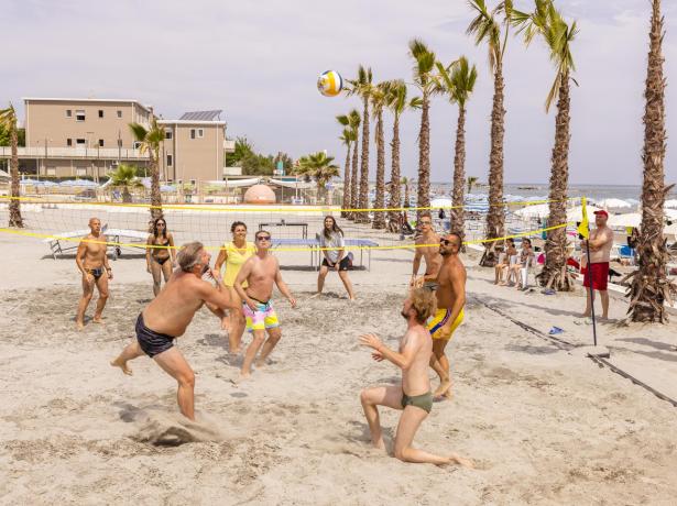 Partita di beach volley su una spiaggia con palme e spettatori.