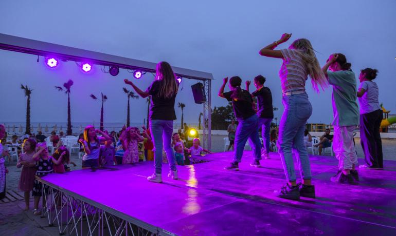 Spettacolo serale sulla spiaggia con bambini e giovani sul palco.