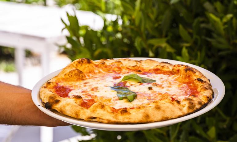 Pizza Margherita con basilico fresco su piatto bianco.