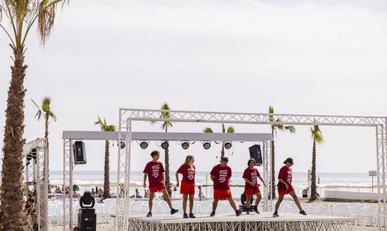 Danseurs sur scène de plage avec des t-shirts rouges.