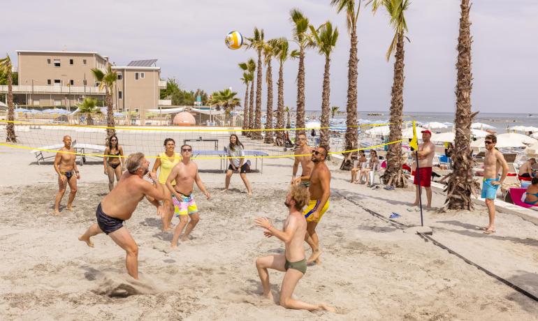 Beachvolleyballspiel am Strand mit Palmen und Zuschauern.