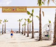 Famiglia cammina sulla spiaggia, tra ombrelloni e sdraio, verso il mare.