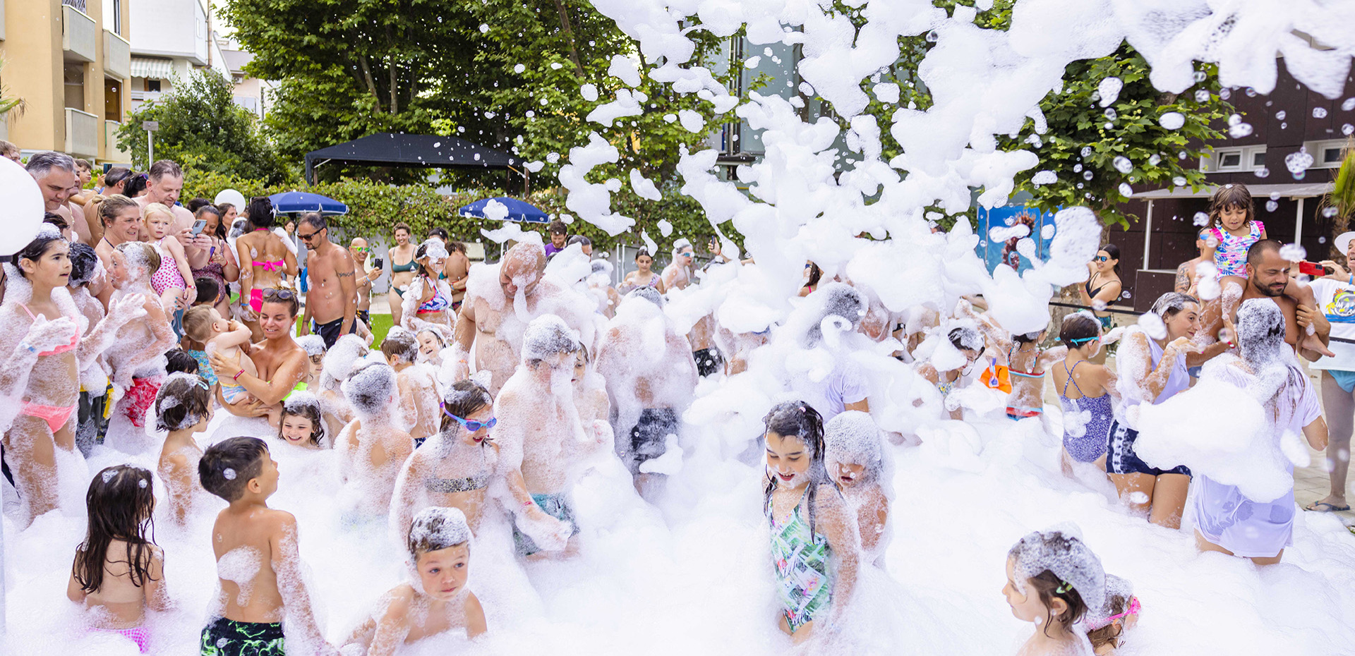 Festa di schiuma all'aperto, bambini e adulti giocano felici.
