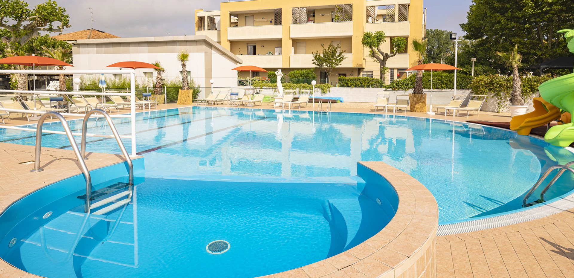 Bambina sorridente in piscina, appoggiata al bordo con acqua scintillante.