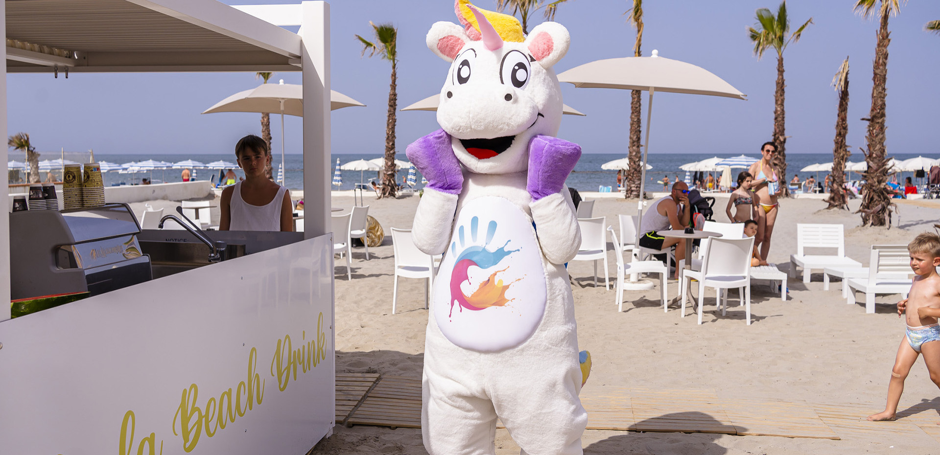 Bambini e adulti sorridenti al mare con bicchieri di plastica colorati.