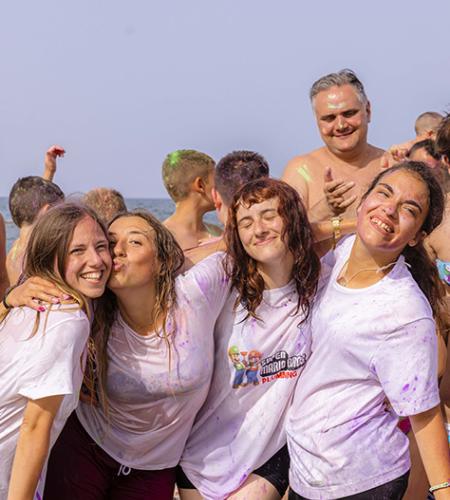 Bambino seduto al tavolo con colori, accompagnato da un adulto sorridente.