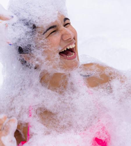 Persone si divertono in una festa di schiuma, sorrisi e bolle ovunque.