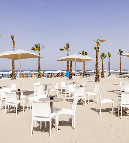 Mann öffnet Sonnenschirm am leeren Strand, blauer Himmel und wiegende Palmen.