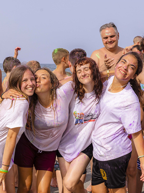 Bambino seduto al tavolo con colori, accompagnato da un adulto sorridente.