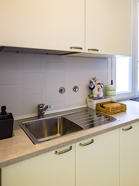 Famiglia in cucina, madre prepara, bambino sorride, altra donna dà da mangiare al piccolo.