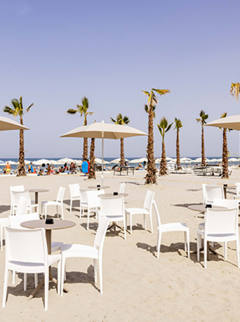 Mann öffnet Sonnenschirm am leeren Strand, blauer Himmel und wiegende Palmen.