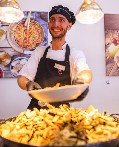 Buffet con piatti caldi e freddi, illuminato da lampade riscaldanti.