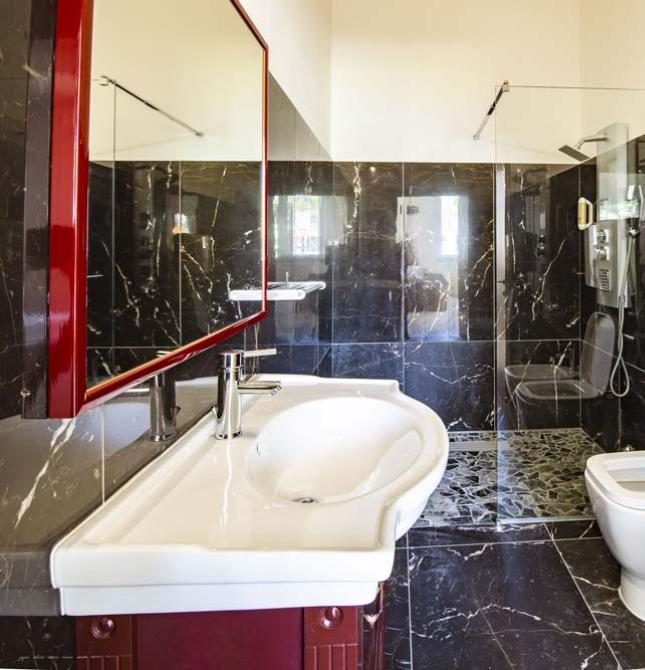 Elegantes Badezimmer mit schwarzem Marmor, weißem Waschbecken und moderner Dusche.